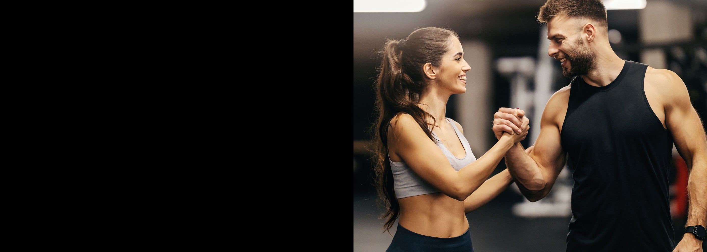 Junge Frau und junger Mann im Fitnessstudio lächeln sich an und schlagen freundschaftlich die Hände ein.