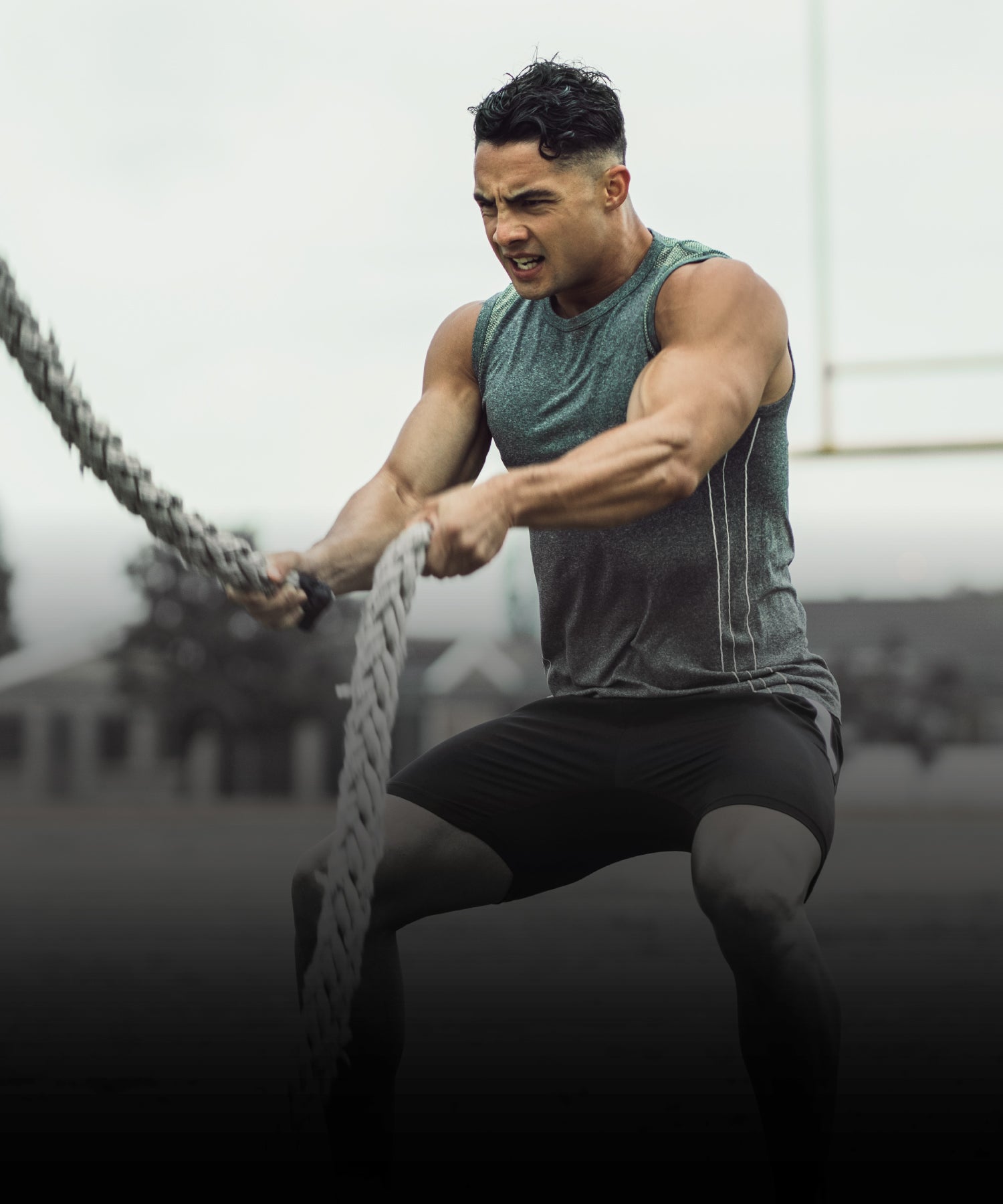 Sportler in ärmellosem Shirt trainiert im Freien mit schweren Battle Ropes und zeigt dabei angespannte Muskelkraft.