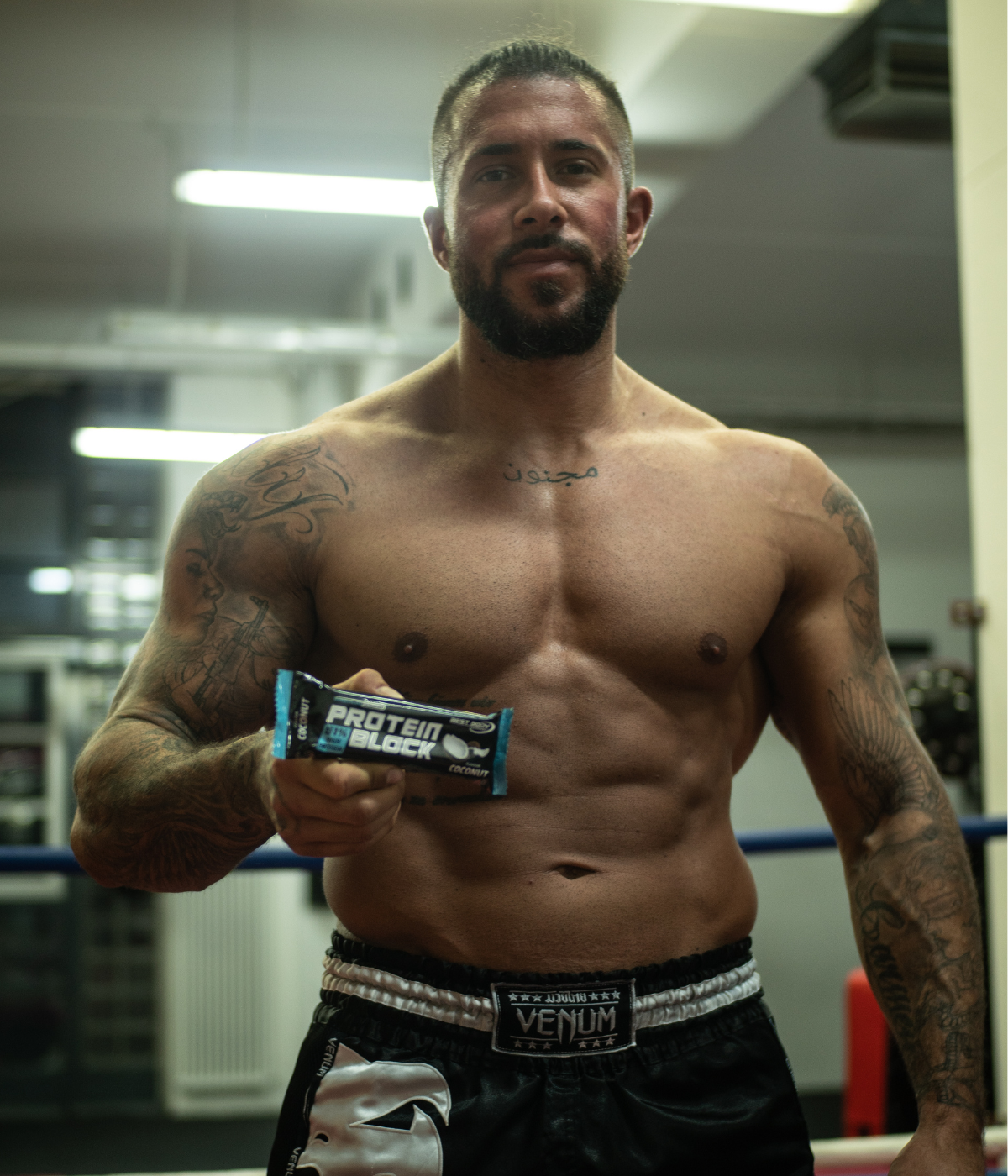 Muskulöser Mann im Fitnessstudio trägt Boxershorts und hält einen Proteinriegel von Best Body Nutrition in der Hand.